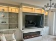 A bespoke fitted media wall with integrated LED lighting, built-in shelving, storage cupboards, electric fire and wall-mounted TV by Dragonville Interiors.