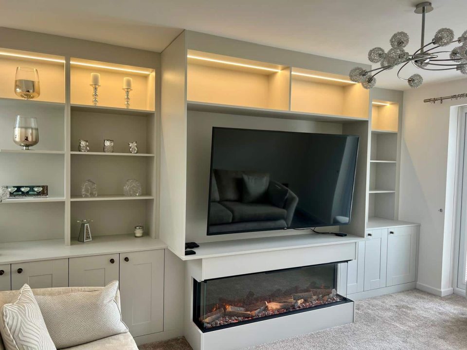 A bespoke fitted media wall with integrated LED lighting, built-in shelving, storage cupboards, electric fire and wall-mounted TV by Dragonville Interiors.